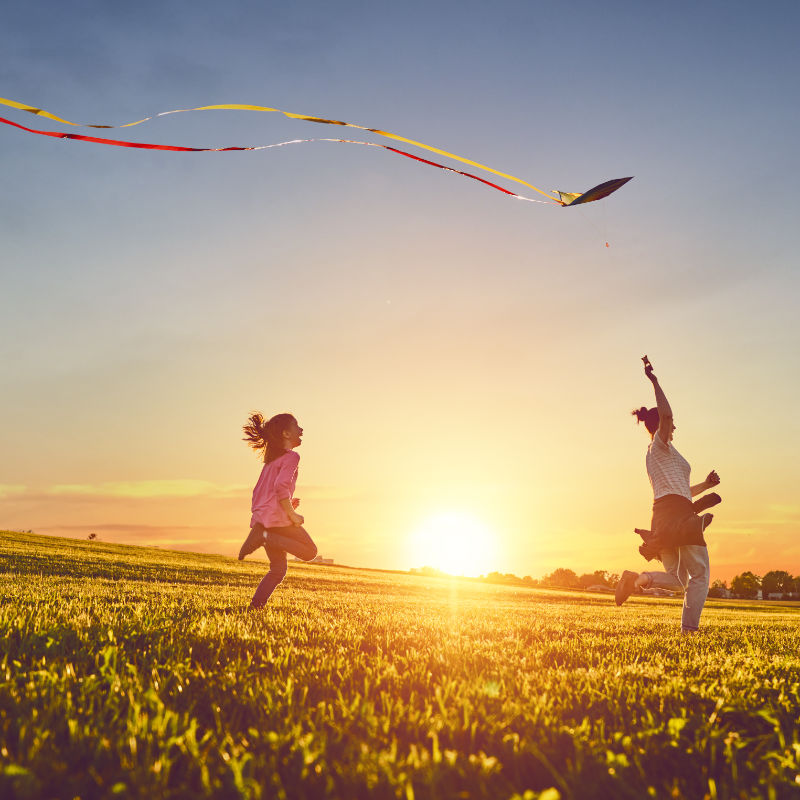 Happy family playing outdoor. Mother and children running on meadow with a kite in the summer on the nature.